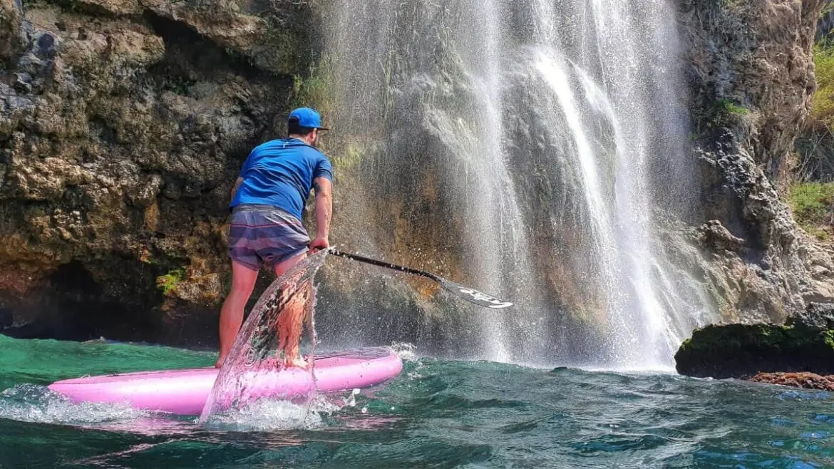 Hombre sobre tabla de padel surf navegando por los acantilados y cascada de Maro en Nerja Malaga