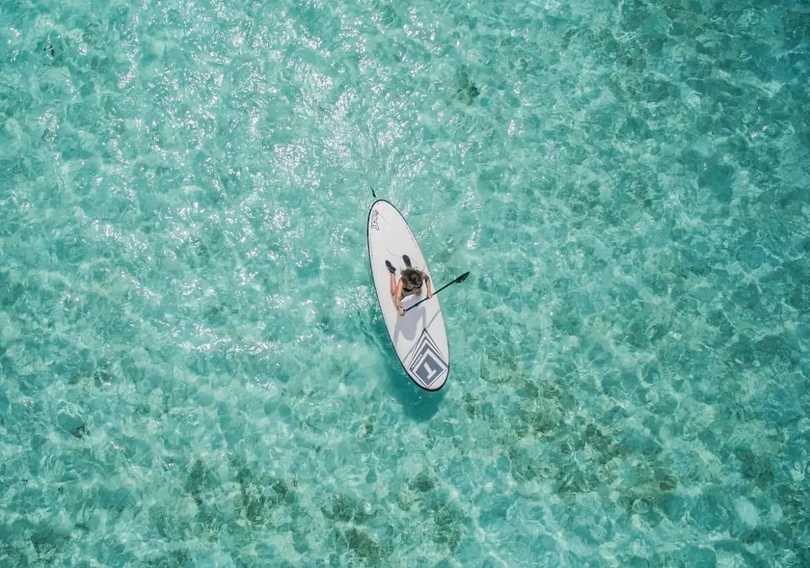 vista-aerea-mujer-sobre-tabla-blanca-de-paddle-surf-en-aguas-cristalinas