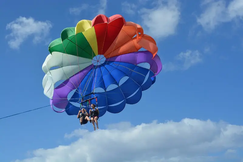 Hombre y Mujer practicando parasailing con un paracaidas multicolor en el mar